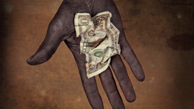 Dark-skinned, possibly malnourished hand holding a crumpled one-dollar note